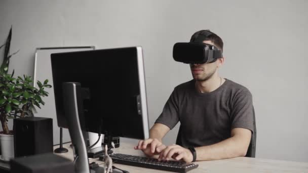 Jeune homme portant des lunettes de réalité virtuelle casque et assis dans le bureau contre ordinateur et dactylographier un texte sur un clavier. Connexion, technologie, nouvelle génération . — Video