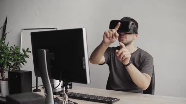 Young man wearing virtual reality goggles headset and sitting in the office against computer and trying to touch objects or control VR with a hand. Connection, technology, new generation. — Stock Video