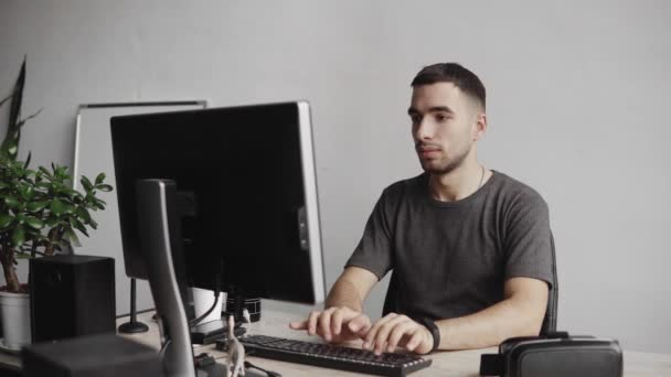 Young man start using virtual reality goggles headset and sitting in the office against computer and trying to touch objects or control VR with a hand. Connection, technology, new generation. — 비디오