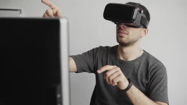 Young man wearing virtual reality goggles headset and sitting in the office against computer and trying to touch objects or control VR with a hand. Connection, technology, new generation. — 비디오