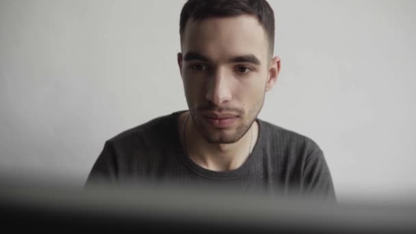 Joven estudiante de negocios o freelancer en una camisa sentada contra monitor de computadora y escribiendo un teclado en una mesa en la oficina con una expresión reflexiva. Trabajando en su portátil en la oficina . — Vídeo de stock