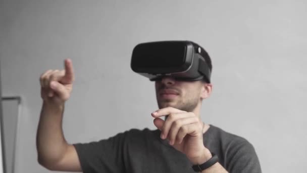 Jongeman draagt een virtual reality bril en zit in het kantoor tegen de computer en probeert objecten aan te raken of Vr met de hand te bedienen. Verbinding, technologie, nieuwe generatie. — Stockvideo