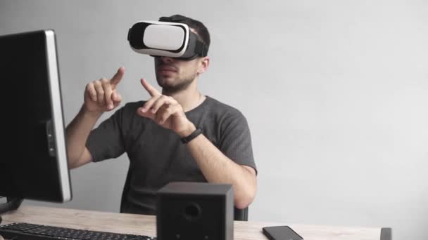 Молодий чоловік в гарнітурі окулярів віртуальної реальності сидить в офісі проти комп'ютера і намагається торкнутися об'єктів або контролювати VR рукою. Зв'язок, технології, нове покоління . — стокове відео