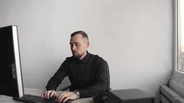 Ung affärsman eller student i en skjorta som sitter mot Monitor av dator. Arbeta på en dator vid ett bord på kontoret med ett tankeväckande uttryck. Ung affärsman som arbetar på sin laptop i Office. — Stockvideo