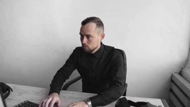 Молодой бизнесмен или студент в рубашке сидит против монитора компьютера. Работа на компьютере за столом в офисе с вдумчивым выражением лица. Молодой бизнесмен, работающий над ноутбуком в офисе . — стоковое видео