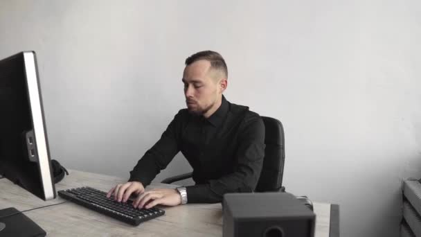 Joven hombre de negocios o estudiante en una camisa sentada contra el monitor de la computadora. Trabajar en una PC en una mesa en la oficina con una expresión reflexiva. Joven hombre de negocios trabajando en su computadora portátil en la oficina . — Vídeo de stock