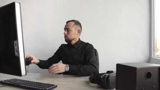 Impresionado feliz sonriente Joven hombre de negocios o estudiante en una camisa sentado contra el monitor de la computadora en los auriculares y empezar a hablar con alguien a través de Internet . — Vídeo de stock