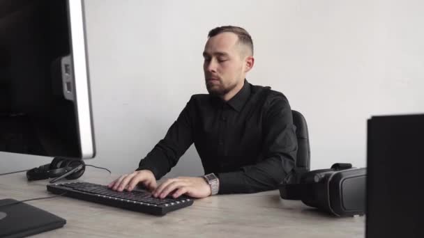 コンピュータのモニターに対して座っているシャツを着た若いビジネスマンや学生。思慮深い表情でオフィスのテーブルでパソコンに取り組む。オフィスでラップトップで働く若いビジネスマン. — ストック動画