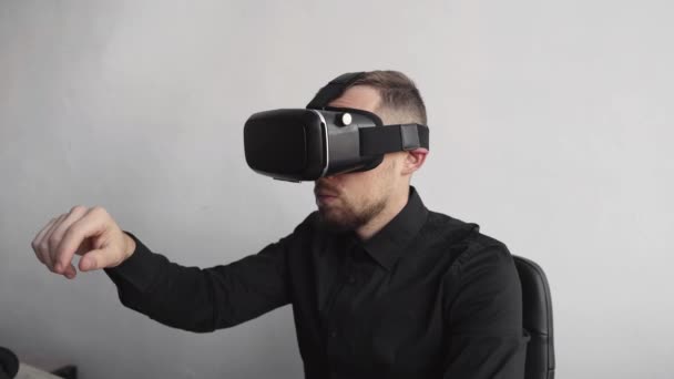 Joven barbudo sentado contra la computadora con gafas de realidad virtual tratando de tocar algo o tocar algo delante de lo que ve. Tecnologías modernas. El concepto de tecnología futura . — Vídeos de Stock