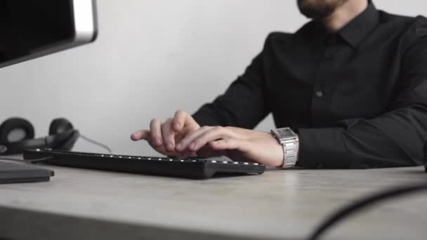 Jovem homem de negócios ou estudante em uma camisa que se senta contra o monitor do computador. Trabalhando em um PC em uma mesa no escritório com uma expressão pensativa. Jovem empresário trabalhando em seu laptop no escritório . — Vídeo de Stock