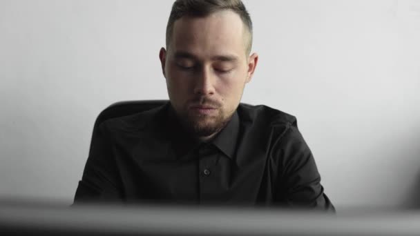 Jonge zakenman of student in een shirt zitten tegen monitor van de computer. Werken op een PC aan een tafel op kantoor met een doordachte uitdrukking. Jonge zakenman werkt op zijn laptop in kantoor. — Stockvideo