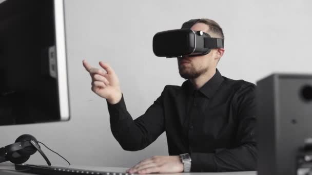 Ung skäggiga man sitter mot datorn med Virtual Reality glasögon försöker röra något eller peka på någon sak framför vad han ser. Modern teknik. Konceptet framtidens teknik. — Stockvideo