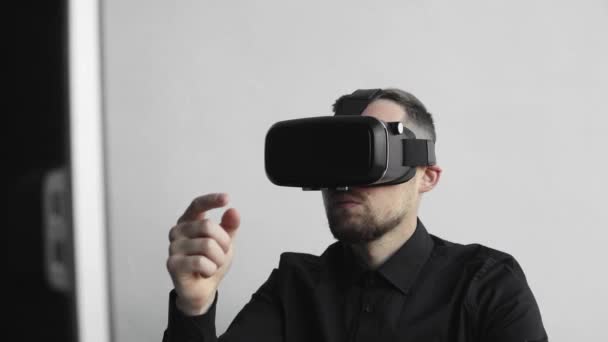 Молодий бородатий чоловік сидить проти комп'ютера з окулярами віртуальної реальності, намагаючись торкнутися чогось або торкнутися чогось перед тим, що він бачить. Сучасні технології. Концепція майбутніх технологій . — стокове відео