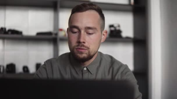 Junger Geschäftsmann oder Student im Hemd sitzt gegen Laptop. Arbeit am PC an einem Tisch im Büro mit nachdenklichem Gesichtsausdruck. Jungunternehmer arbeitet im Büro an seinem Laptop. — Stockvideo