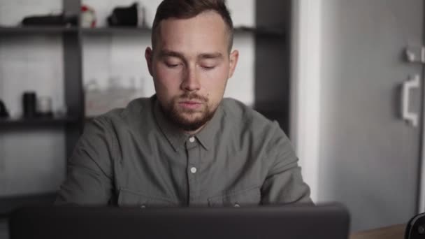 Joven hombre de negocios o estudiante en una camisa sentada contra el portátil. Trabajar en una PC en una mesa en la oficina con una expresión reflexiva. Joven hombre de negocios trabajando en su computadora portátil en la oficina . — Vídeos de Stock