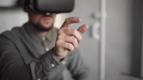 Jonge bebaarde man zitten tegen computer met Virtual reality bril proberen om iets aan te raken of tik op een ding in de voorkant van wat hij ziet. Moderne technologieën. Het concept van toekomstige technologie. — Stockvideo