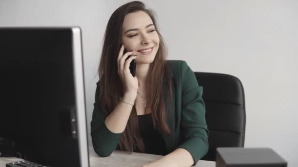 Porträt einer jungen Geschäftsfrau, die im weißen Büro gegen den Computerbildschirm telefoniert. Unternehmerin mit Anruf und Arbeit mit dem Computer am Tisch sitzend.. — Stockvideo