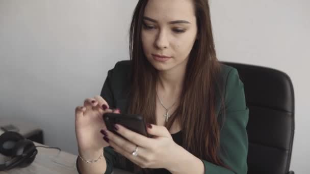 Beyaz ofisteki bilgisayar ekranında telefonu kullanan genç bir iş kadınının portresi. Kadın girişimci sohbet ediyor ve masada oturan bilgisayarla çalışıyor. Telefon konuşmaları.. — Stok video