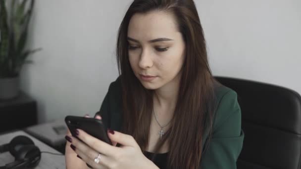 Retrato de una joven mujer de negocios usando el teléfono contra la pantalla de la computadora en la oficina blanca. Emprendedora conversando y trabajando con computadora sentada en la mesa. Trabajo telefónico chateando . — Vídeo de stock