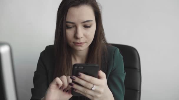 Portrait de jeune femme d'affaires utilisant le téléphone contre l'écran d'ordinateur dans le bureau blanc. Femme entrepreneure ayant une conversation et travaillant avec un ordinateur assis à table. Travail téléphonique bavardage . — Video