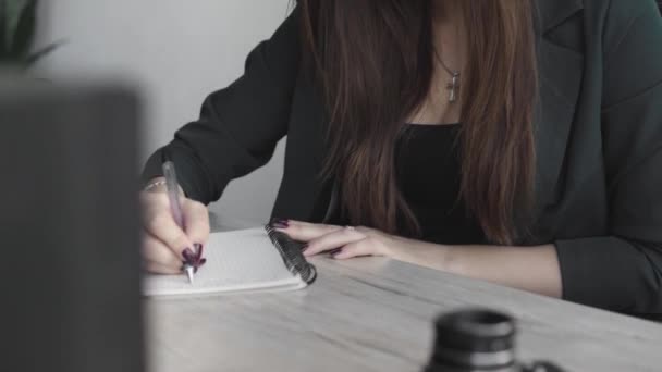 Una mujer de negocios escribiendo algo en un cuaderno. Mujer emprendedora estudiante que estudia escritura nota en el lugar de trabajo cerca de la computadora. Una mano de mujer apuntando en un cuaderno blanco en la mesa . — Vídeos de Stock