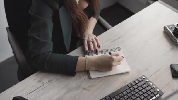 Una mujer de negocios escribiendo algo en un cuaderno. Mujer emprendedora estudiante que estudia escritura nota en el lugar de trabajo cerca de la computadora. Una mano de mujer apuntando en un cuaderno blanco en la mesa . — Vídeos de Stock