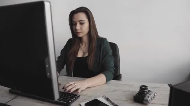 Mujer morena está trabajando delante de un monitor en una oficina. Mujer de negocios trabajando en la computadora en el espacio de coworking. Retrato de la señora feliz escribiendo en el lugar de trabajo. Profesional femenino trabajando con pc . — Vídeos de Stock