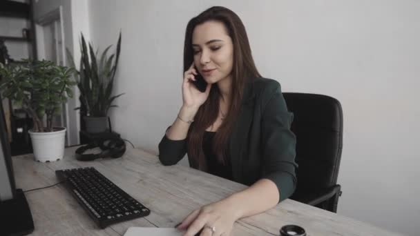 Retrato de una joven mujer de negocios hablando de teléfono contra la pantalla de la computadora en la oficina blanca. Emprendedora que tiene llamada y trabaja con computadora sentada en la mesa.Teléfono llamada de trabajo . — Vídeos de Stock