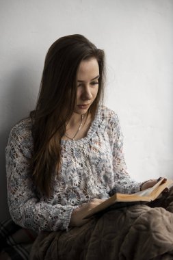 Çekici genç bayan, evin pencere eşiğinde kitap okuyor. Büyük pencere, yeşil bitkiler..