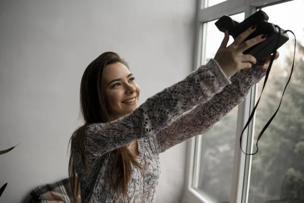 Sorrindo jovem morena tira fotografias selfie retrato com câmera de foto velha . — Fotografia de Stock