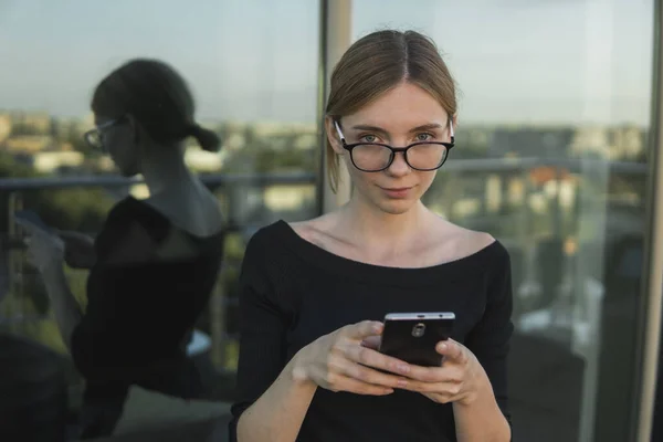 Young business woman uses phone. Good looking brunette female uses online banking on smart phone to transfer money from credit card. Girl using smart phone and chatting with business partners.