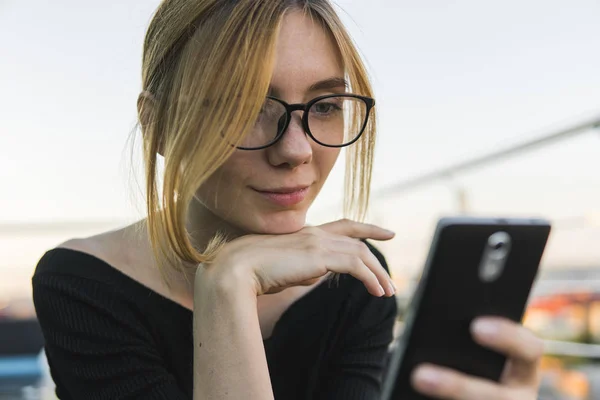 Young business woman uses phone. Good looking brunette female uses smart phone chatting with business partners or friends.