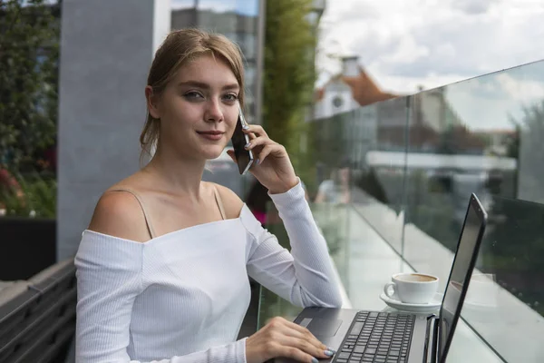 Woman working on laptop at office while talking on phone. Portrait of young smiling business woman calling her best friend, having break, telling something funny, sitting in cafe. — Stock Photo, Image