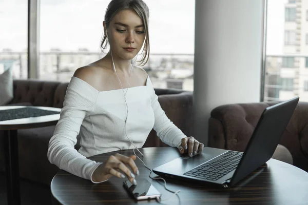 Jonge zakenvrouw die laptopcomputer gebruikt in café of in coworking en sms 'en op een smartphone. Blond vrouwtje werkend op laptop in een outdoor cafe. — Stockfoto