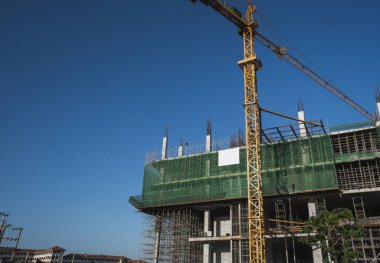 Mavi gökyüzüne karşı vinç ve inşaat alanı. İnşaatın bitmemiş binasının metal inşaatı. Crane kulesi çok katlı depo inşaatı için kullanılıyor.