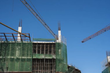 Mavi gökyüzüne karşı vinç ve inşaat alanı. İnşaatın bitmemiş binasının metal inşaatı. Crane kulesi çok katlı depo inşaatı için kullanılıyor.