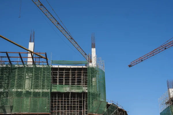 Żuraw i budowa placu budowy przed błękitnym niebem. Metalowa konstrukcja niedokończonego budynku na budowie. Zastosowanie żurawia wieżowego do budowy budynku wielo-magazynowego. — Zdjęcie stockowe