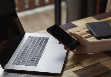 Kadın eli bilgisayarlı akıllı telefon kullanır. İnternette çalış ve çalış, serbest çalış. Serbest çalışan ya da serbest çalışan bir kadın, dizüstü bilgisayarıyla çalışan bir kız ahşap masada oturan bir telefon ve okuyucu..