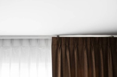 Kahverengi perdeler ve beyaz tavanlı bir ray üzerinde beyaz tül. Oturma veya uyku odasında perde iç dekorasyon. Kendi evinde rahat bir yaşam. Tatlı confy ev.