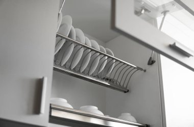 Bulaşık kurutucu metal raf ve büyük beyaz tabaklar. Geleneksel rahat mutfak. İçinde ıslak cam ve seramik tabaklar, tabaklar ve kaseler olan beyaz tabak kurutma dolabını aç..