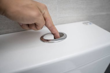 Close up of finger pushing a flush toilet button for cleaning a toilet. clipart