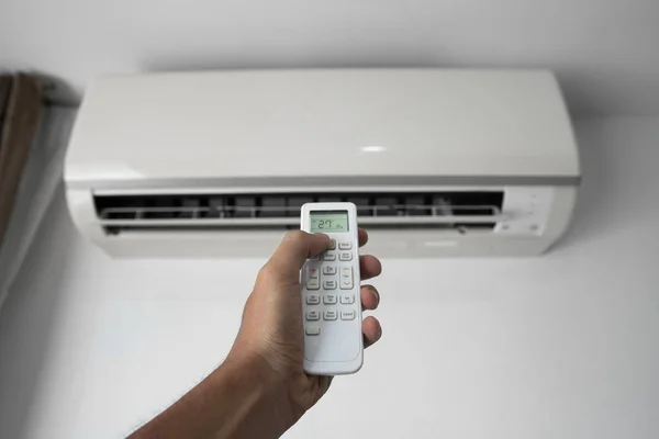 Mans hand using remote controler. Hand holding rc and adjusting temperature of air conditioner mounted on a white wall. Indooor comfort temperature. Health concepts and energy savings.