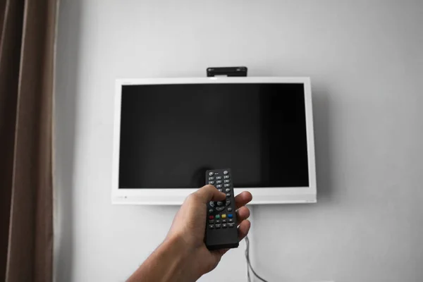 The man with the remote control in hand want switch on the TV and presses the button on the remote control. Remote control in hand closeup. — Stock Photo, Image