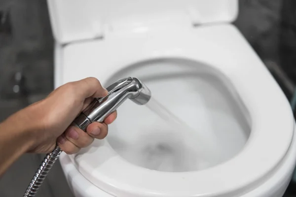 Použití bidetové sprchy s bílým WC. Bidet sprcha v mužské ruce pro použití s bílou toaletní mísou. — Stock fotografie