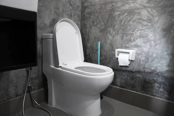 家庭浴室白色马桶上的白色悬挂马桶座，有混凝土风格的灰色瓷砖，墙上有卫生纸。浴室豪华内饰. — 图库照片