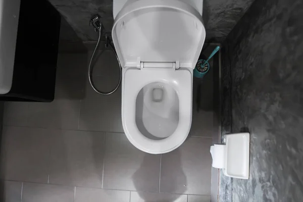 Sedile WC bianco appeso sulla toilette bianca nel bagno di casa con piastrelle grigie in stile cemento e carta igienica sulla parete. Bagno interno di lusso . — Foto Stock