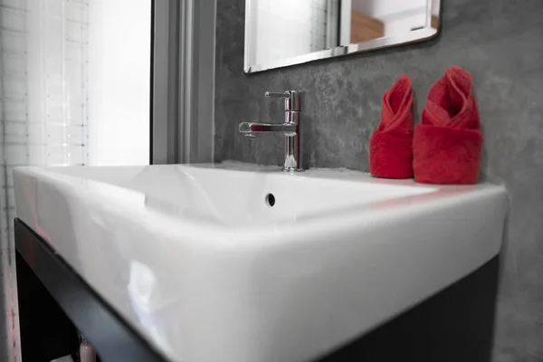 Современный кран из нержавеющей стали с умывальником с двумя красными полотенцами на нем. Интерьер в ванной комнате современный. Роскошная и стильная ванная комната с бетонными стенами . — стоковое фото