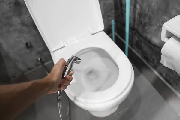 Utilisation d'une douche bidet avec toilettes blanches. Douche Bidet à la main masculine pour utilisation avec un bol de toilette blanc . — Photo