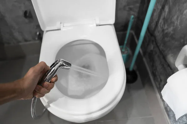 Using of bidet shower with a white toilet. Bidet shower in male hand for using with a white toilet bowl. — ストック写真