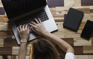 Kadın elleri dizüstü bilgisayarda klavye üst görünümünde yazı yazıyor. İnternette çalış ve çalış, serbest çalış. Serbest çalışan ya da serbest çalışan bir kadın, dizüstü bilgisayarıyla çalışan bir kız ahşap masada oturan bir telefon ve okuyucu..